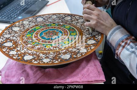 Ein talentierter Handwerker, der in seiner Werkstatt an farbenfrohen Holzplatten arbeitet, als Souvenir für den Souvenirladen Stockfoto