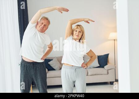 Ich mache Dehnübungen. Seniorenmann und -Frau sind zu Hause zusammen Stockfoto