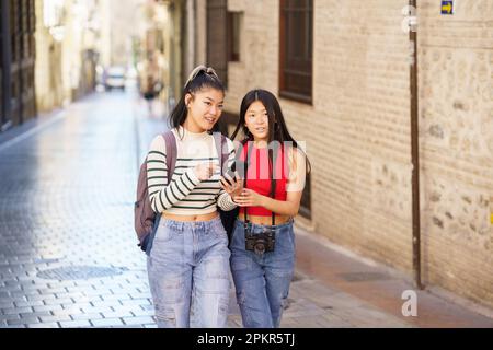 Asiatische weibliche Touristen, die mit dem Smartphone auf der Straße der Stadt spazieren gehen Stockfoto