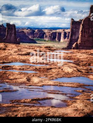 Pfützen füllen die Konturen der Felsoberfläche mit Blick auf Courthouse Wash im Arches National Park, Utah. Stockfoto