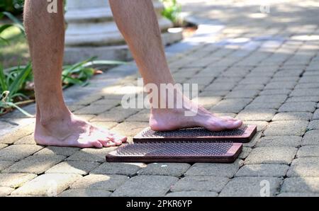Alternative Medizin und Achtsamkeitspraxis, Nadel steht auf einem Sadhu-Brett, barfuß. Stockfoto