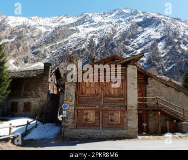 Traditionelles Holz- und Steingebäude unter einem schneebedeckten Berg in Valnoney im Gran Paradiso Nationalpark, Aosta Valley, Italien Stockfoto