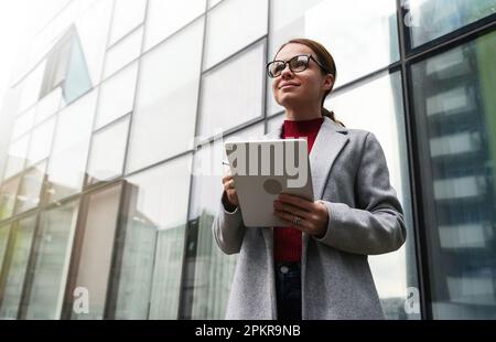 Erfolgreiche Geschäftsfrau mit einem digitalen Tablet in den Händen, die neben dem Bürogebäude steht. Stockfoto