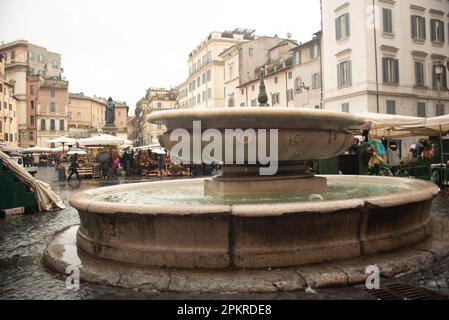 Römischer Brunnen in Campo de' Fiori mit traditionellem Blumenmarkt, der heute ein Bauernmarkt ist, im Hintergrund Stockfoto