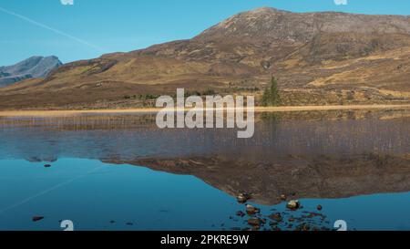 Blick auf die Isle of Skye über loch zu Bergen im Hintergrund mit Reflexionen von Bergen und Bäumen im loch an einem hellen morgen im februar. Stone in Stockfoto