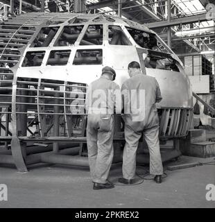 1950er, historisch, Luftfahrt, zwei männliche Mechaniker in Overalls, die an der Außenseite eines Flugzeugcockpits in einer Luft- und Raumfahrtfabrik oder einem Aufhänger arbeiten, Short Bros, England, Großbritannien. Stockfoto