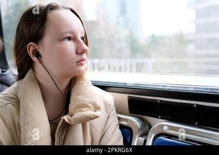 Junge Teenager, die im Transport mitfährt, schaut aus dem Fenster Kopfhörer Mobiltelefon friedliche Gesichtsfläche für Text Sky Train Bus Auto gewöhnliche Person in echten Straßen Städte kanada Vorort surrey Stockfoto