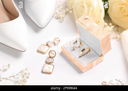 Box mit Eheringen, Ohrringen, Absätzen und Blumen auf weißem Hintergrund, Nahaufnahme Stockfoto
