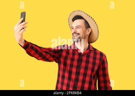 Ein gutaussehender Mann mit Handy, der Selfie auf gelbem Hintergrund macht. Festa Junina (Juni-Festival) Stockfoto