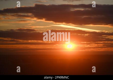 Sonnenuntergang am Himmel mit rotem Licht der untergehenden Sonne. Abendwolken im orangefarbenen Licht der Sonnenuntergangsstrahlen Stockfoto