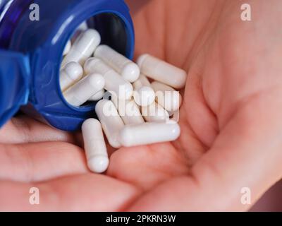 Eine Frau gießt Dimethylaminoethanolbitartrat-Kapseln (DMAE) aus einer Flasche in die Handfläche. Schließen. Stockfoto