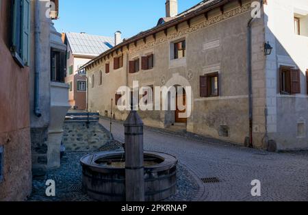 Dorf Guarda (1.653 m), Niederengadin, Graubünden, Schweiz: Alte Häuser (eines mit Inschrift) und Brunnen entlang der Chasa, der Hauptkopfsteingepflasterstraße Stockfoto