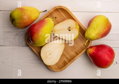 Vier ganze und zwei Hälften Bio-Birnen auf einem Bambusblech, auf einem weißen Holztisch, Draufsicht. Stockfoto