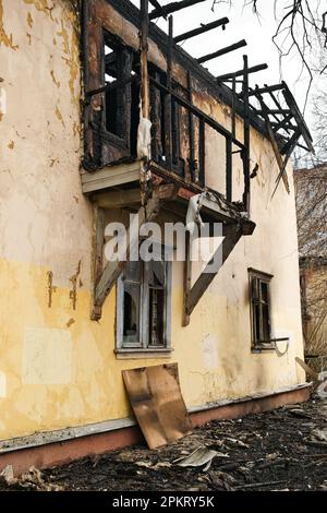 Fassade eines alten zweistöckigen Hauses nach einem Brand. Verbranntes Wohngebäude. Außenansicht des zerstörten Hauses. Stockfoto