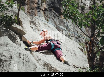 Lächelnde athletische Frau in Schutzhelm Klettern Klippe Felswand mit Top-Seil und Klettergurt in Paklenica Nationalpark-Website in Kroatien. A Stockfoto