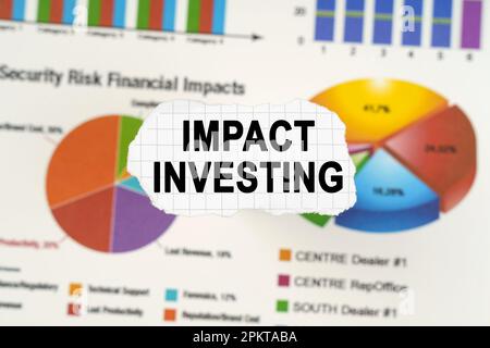 Geschäftskonzept. Auf Diagrammen und Diagrammen liegt zerrissenes Papier mit der Aufschrift „Impact Investing“. Diagramme und Diagramme sind verschwommen. Stockfoto