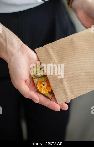 In den Händen einer Frau ist eine Papiertüte mit kandierten Früchten. Nahaufnahme. Stockfoto
