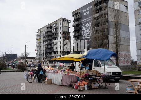 Ein Einwohner von Borodyanka sah, wie er Lebensmittel auf dem Hauptplatz von Borodyanka, Ukraine, neben einem zerstörten Gebäude mit einem Plakat mit der Aufschrift „Kick Russia out of the UN“ kaufte. Trotz der einjährigen Befreiung von Borodyanka, einer Stadt nordwestlich der ukrainischen Hauptstadt Kiew, sind die Bewohner von Borodyanka nicht zur Normalität zurückgekehrt. Der Wiederaufbauprozess verlief stetig, aber langsam, zerstörte Gebäude bleiben im Stadtzentrum. Viele Bewohner leben in beschädigten Gebäuden, die jetzt teilweise repariert sind, während andere, die ihr Zuhause verloren haben, immer noch in provisorischen Wohnungen leben. Die Beamten sind noch unsicher Stockfoto