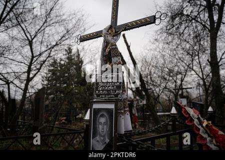 6. April 2023, Borodyanka, Ukraine: Ein Kreuz, ein Porträt und Schriften, die auf einem Friedhof in Borodyanka zu sehen sind und lesen: "Tot gestorben nach der russischen Invasion im letzten Jahr". Trotz der einjährigen Befreiung von Borodyanka, einer Stadt nordwestlich der ukrainischen Hauptstadt Kiew, sind die Bewohner von Borodyanka nicht zur Normalität zurückgekehrt. Der Wiederaufbauprozess verlief stetig, aber langsam, zerstörte Gebäude bleiben im Stadtzentrum. Viele Bewohner leben in beschädigten Gebäuden, die jetzt teilweise repariert sind, während andere, die ihr Zuhause verloren haben, immer noch in provisorischen Wohnungen leben. Die Beamten sind sich noch nicht sicher Stockfoto