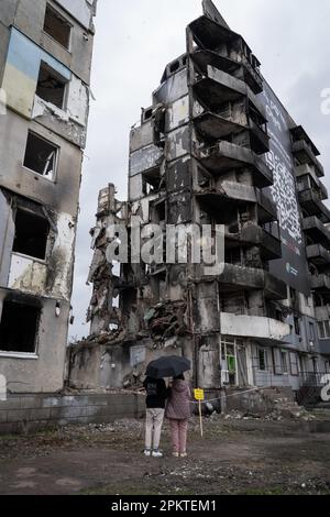 Borodyanka, Ukraine. 6. April 2023. Die Bewohner von Borodyanka sahen, wie sie Fotos von der Arbeit des weltberühmten Graffiti-Künstlers Banksy an einem zerstörten Gebäude machten. Trotz der einjährigen Befreiung von Borodyanka, einer Stadt nordwestlich der ukrainischen Hauptstadt Kiew, sind die Bewohner von Borodyanka nicht zur Normalität zurückgekehrt. Der Wiederaufbauprozess verlief stetig, aber langsam, zerstörte Gebäude bleiben im Stadtzentrum. Viele Bewohner leben in beschädigten Gebäuden, die jetzt teilweise repariert sind, während andere, die ihr Zuhause verloren haben, immer noch in provisorischen Wohnungen leben. Die Beamten sind noch unsicher mit dem Zeitlimit Stockfoto