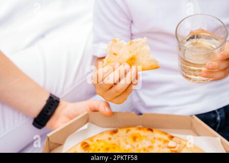 Pizza-Picknick. Mom und Sohn essen Pizza. Köstliche Pizza, vier Käsesorten mit Cheddar, Parmesan, Mozzarella und Tomatensauce Stockfoto