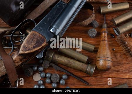 Antike 16-Gauge Break-Action glatt gebohrte Schrotflinte mit Messinggehäuse und Zubehör für Patronennachladung auf Holztisch. Stockfoto