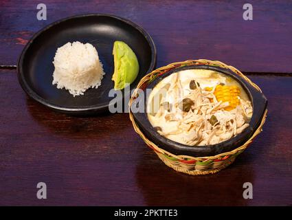 Ajiaco, traditionelles kolumbianisches Essen, begleitet von Reis, Milchcreme, Avocado, Kapern und Salat Stockfoto