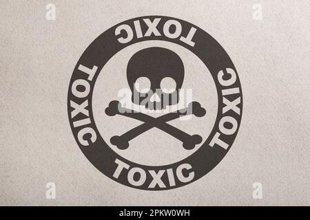 Warnschild (Schädel- und Querlenkersymbol und Wort „GIFTIG“) auf Papier, Draufsicht Stockfoto