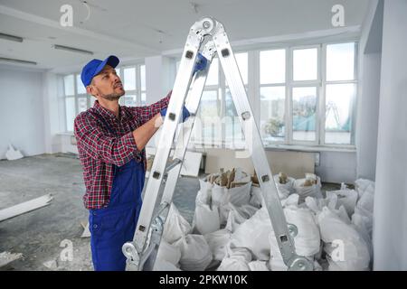 Bauarbeiter, der im Zimmer eine Treppenleiter hochklettert, ist auf die Renovierung vorbereitet Stockfoto