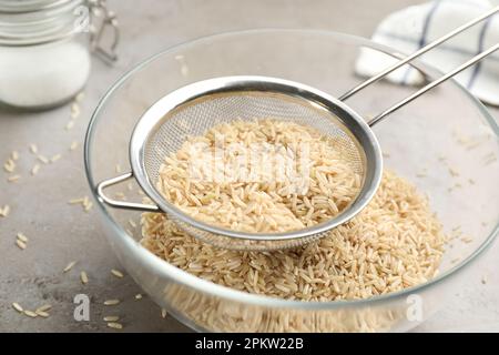 Reis in Schüssel auf grauem Tisch sieben, Nahaufnahme Stockfoto