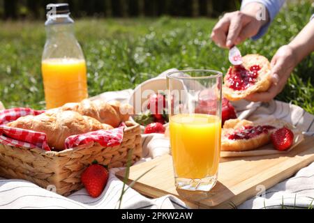 Frau mit Croissants im Freien, konzentriere dich auf ein Glas Saft. Sommerpicknick Stockfoto