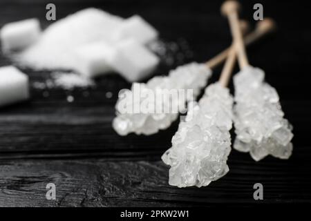 Stäbchen mit Zuckerkristallen auf schwarzem Holztisch, Nahaufnahme. Leckere Rock-Bonbons Stockfoto