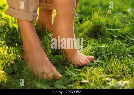 Eine Frau mit ihrem Kind, die barfuß auf grünem Gras im Freien läuft, Nahaufnahme Stockfoto