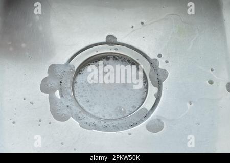 Wasser mit Seifenschaum im Stahlwaschbecken läuft ab Stockfoto
