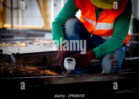 Junger asiatischer Arbeiter, der Schleifeisen mit Händen verwendet, die in einer Industriefabrik arbeiten, Schweißer oder Arbeiter schneiden Stahl, während er funkelnde, berufliche Tec hat Stockfoto