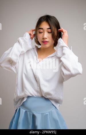 1/2 Half Body Porträt einer jungen asiatischen Frau in einem kurzen blauen Rock und einer weißen Langarmbluse | Weißer Hintergrund | Happy Stockfoto