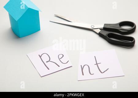 Das Wort "Rent" steht auf Papier und wird mit einer Schere in zwei Hälften geschnitten. Draufsicht Stockfoto