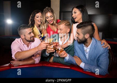 Wunderschönes und gut gekleidetes Paar, das Roulette im Casino spielt und Alkohol trinkt, um zu feiern Stockfoto
