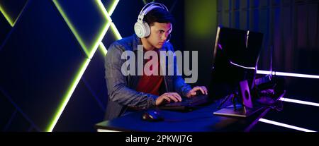Online-Gamer, die in einem fesselnden Videospiel navigieren. Mit einem Headset für die Kommunikation mit seinen Mitspielern konzentriert sich der junge Mann voll und ganz auf seinen PC Stockfoto