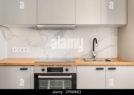 Teil einer Küche in grauen, einfarbigen Farben mit komfortablen Wandschränken und modernen Geräten in einem neuen Apartment. Das Konzept der Renovierung danach Stockfoto