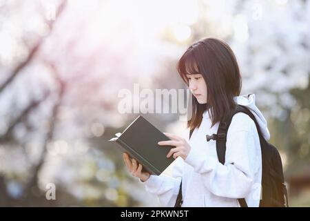 Eintrittszeit Frühjahrsschülerin, High School Student und College Student Konzept mit Rucksack Lesen vor Kirschblüten Bäumen Stockfoto