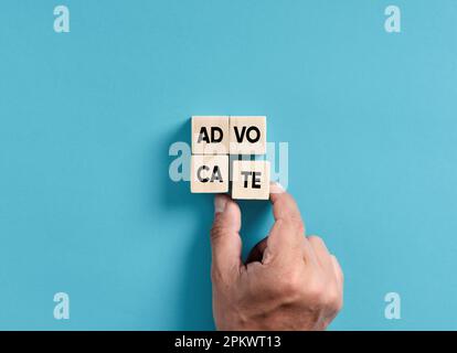Male hand placing wooden blocks into a square shape to assemble the word advocate. Stockfoto