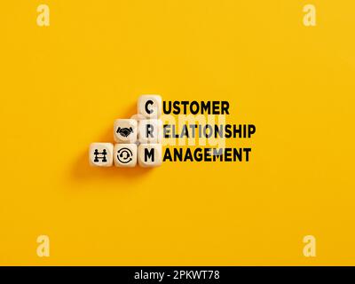 Das Akronym „CRM and Customer Relationship Management“ auf Holzwürfeln auf gelbem Hintergrund. Stockfoto