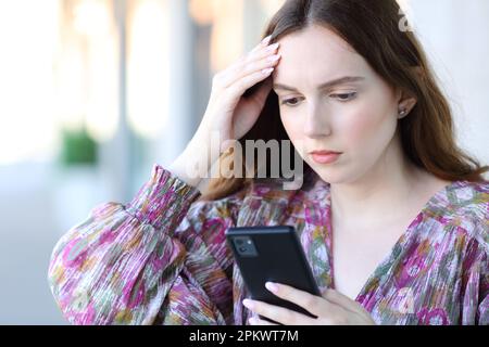 Besorgte Frau, die auf der Straße mit dem Smartphone steht Stockfoto