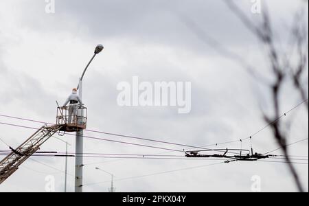 Arbeiter in einer Wiege auf einem Laternenpfahl. Der Elektriker arbeitet an einer Stange Stockfoto