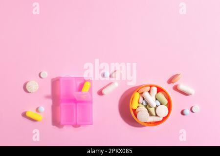 Draufsicht von pharmazeutischen Medikamentenpillen, Tabletten, Kapseln, Nahrungsergänzungsmitteln und Tablettenbox auf hellrosa Hintergrund mit Kopierbereich. Stockfoto