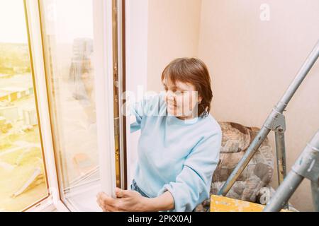 Das Konzept Der Aktiven Senioren. Happy Shy Fröhlich Lächelnd Mature Woman Putzfenster. Der Begriff Haushalt Und Rentner. Weiße Frau Mitte Stockfoto