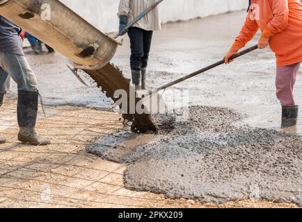 Die Arbeiter gießen den Beton für den Straßenbau mit mobilen Betonmischern. Stockfoto