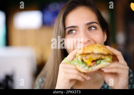 Vorderansicht einer glücklichen Frau, die einen großen Burger in einem Restaurant isst Stockfoto