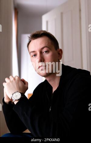 Ein junger blonder Mann in einem schwarzen Pulli allein in seiner Wohnung Stockfoto